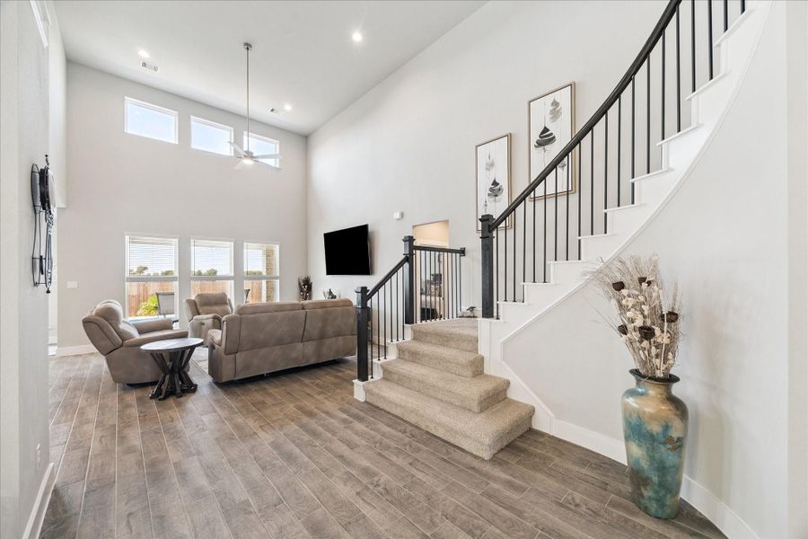 Spacious living room with soaring ceilings, large windows, and an open staircase with wrought-iron railing. Spacious living room with soaring ceilings, large windows, and an open staircase with wrought-iron railing.