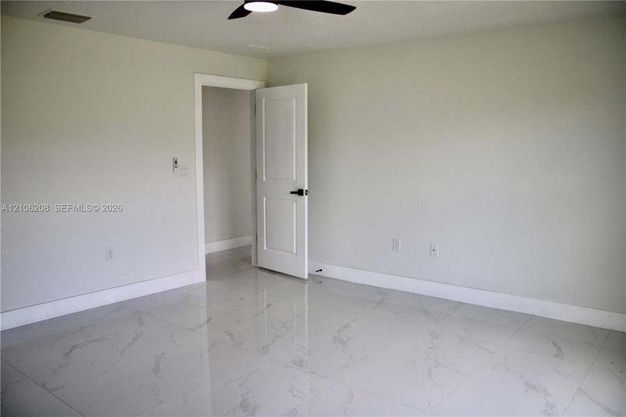 Interior room featuring light-toned, large-format tile flooring with a subtle veined pattern, a two-panel interior door with matte black hardware, and a ceiling-mounted matte black fan