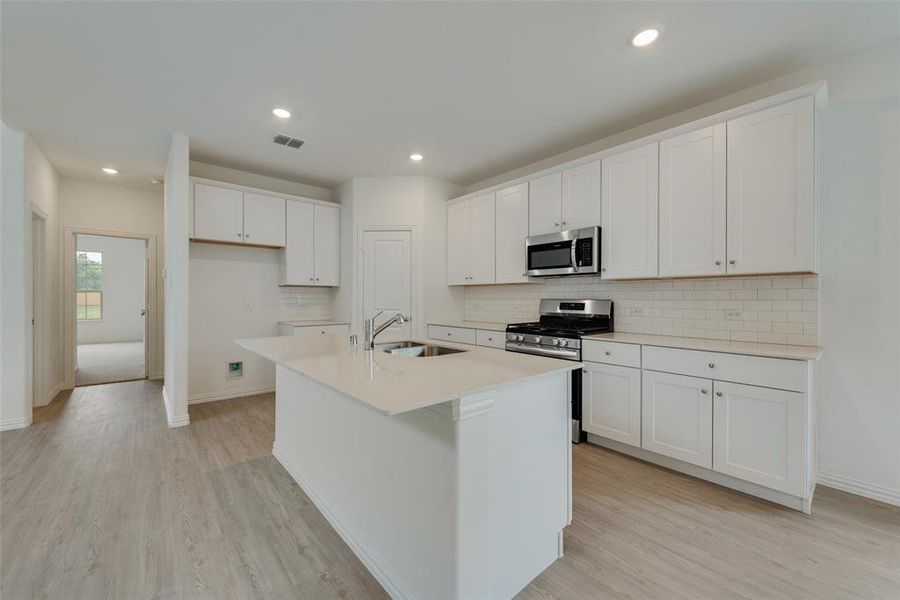 Kitchen with stainless steel appliances, light wood-type flooring, tasteful backsplash, and sink