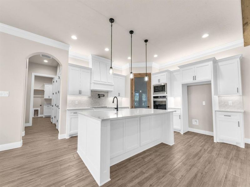 Kitchen with appliances with stainless steel finishes, decorative light fixtures, a center island with sink, white cabinets, and light hardwood / wood-style floors