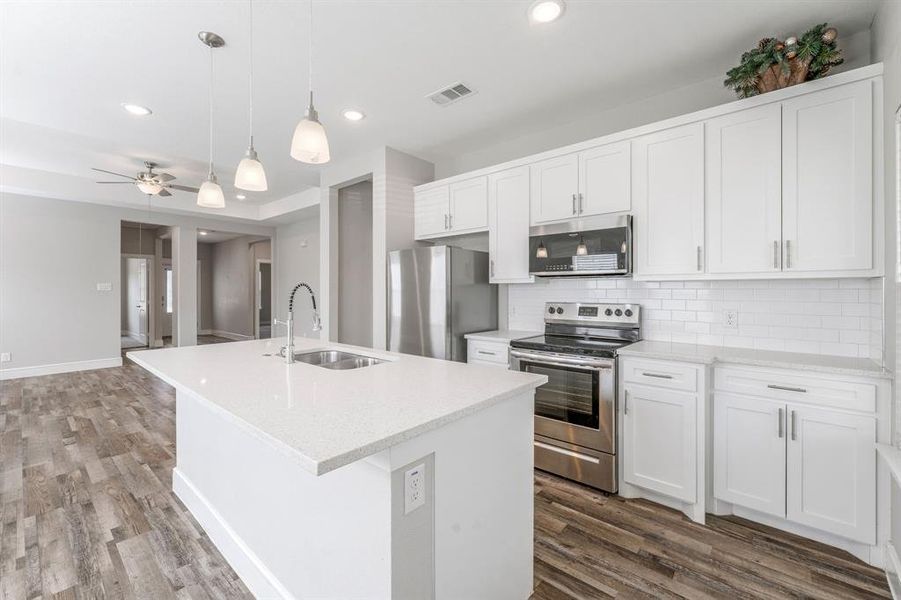 Kitchen with tasteful backsplash, appliances with stainless steel finishes, a kitchen island with sink, white cabinets, and decorative light fixtures Kitchen with tasteful backsplash, appliances with stainless steel finishes, a kitchen island with sink, white cabinets, and decorative light fixtures