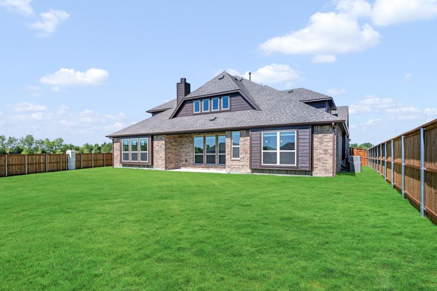 Rear view of brick home with large fenced backyard, green lawn, and multiple large windows Rear view of brick home with large fenced backyard, green lawn, and multiple large windows