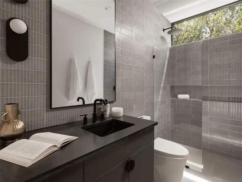 A sleek, contemporary third bathroom features a rainfall shower and a dark vanity with integrated sink. A sleek, contemporary third bathroom features a rainfall shower and a dark vanity with integrated sink.