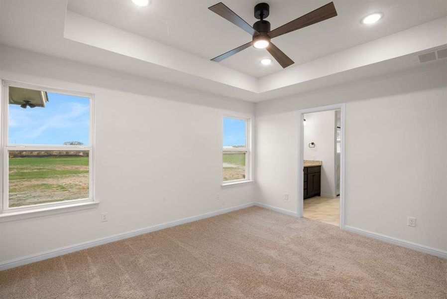 Unfurnished room with a tray ceiling, ceiling fan, and light colored carpet Unfurnished room with a tray ceiling, ceiling fan, and light colored carpet