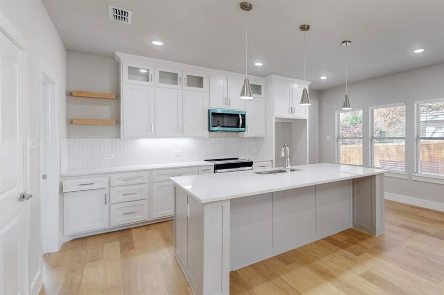 Kitchen featuring a kitchen island with sink, sink, decorative light fixtures, white cabinetry, and stainless steel appliances