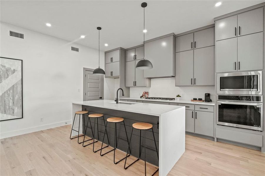 Kitchen featuring appliances with stainless steel finishes, light hardwood / wood-style floors, a kitchen island with sink, sink, and gray cabinets