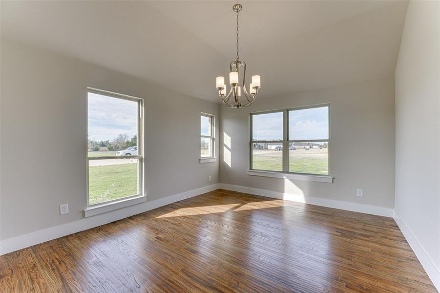 Empty room with a notable chandelier, dark hardwood / wood-style flooring, and lofted ceiling