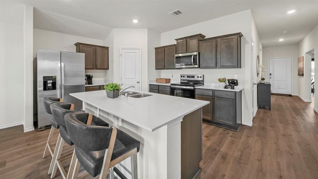 Kitchen with appliances with stainless steel finishes, dark brown cabinets, a breakfast bar, a kitchen island with sink, and recessed lighting Kitchen with appliances with stainless steel finishes, dark brown cabinets, a breakfast bar, a kitchen island with sink, and recessed lighting