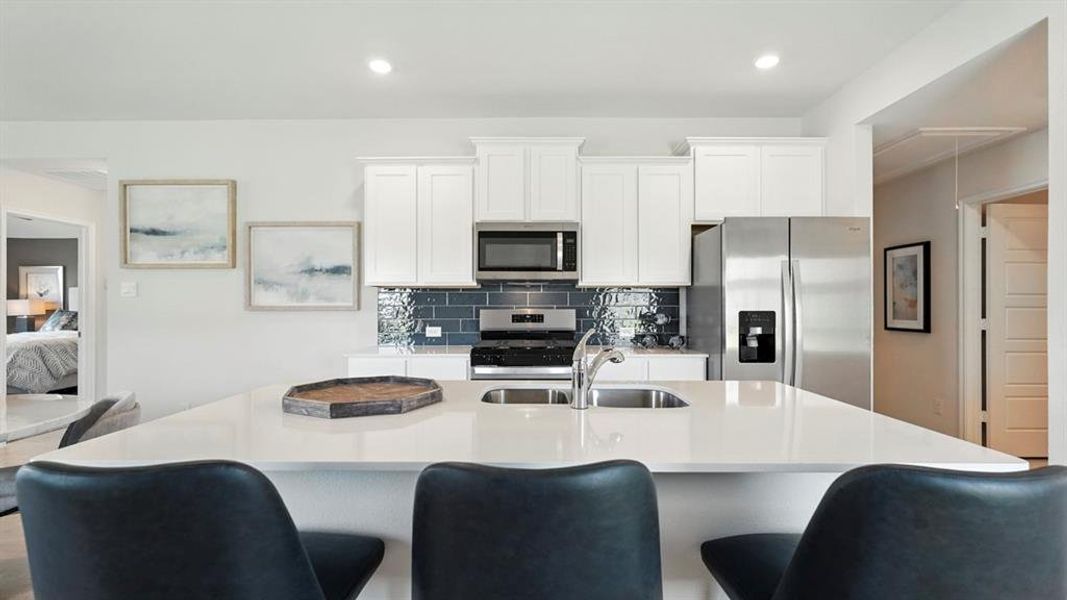 Kitchen with white cabinetry, stainless steel appliances, decorative backsplash, a kitchen breakfast bar, and a kitchen island with sink