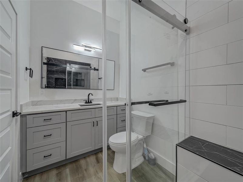 Bathroom featuring tiled shower, hardwood / wood-style flooring, toilet, and vanity