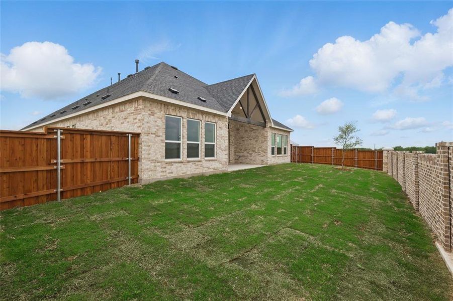 Rear view of property with brick siding, a fenced backyard, roof with shingles, and a lawn