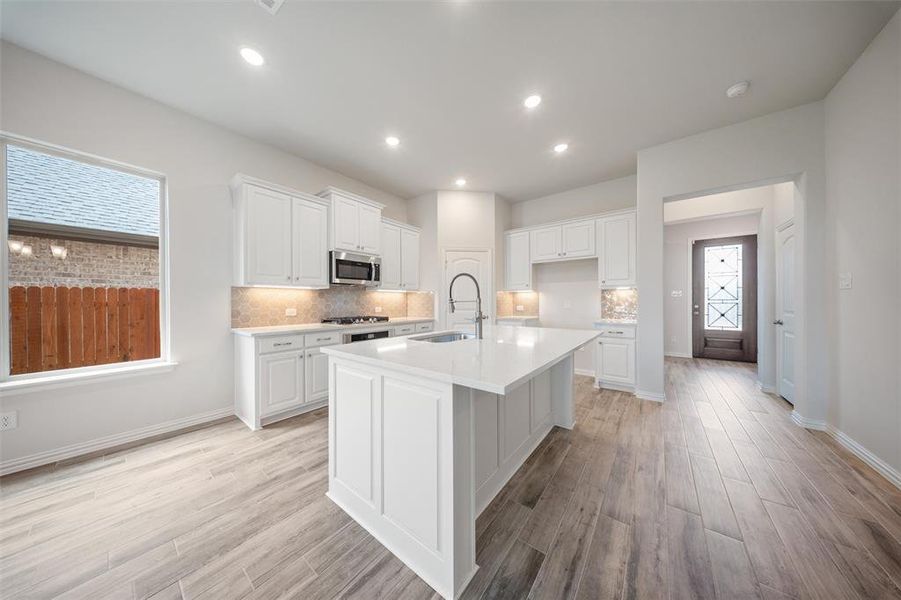 Kitchen featuring light wood-type flooring, light countertops, backsplash, and recessed lighting