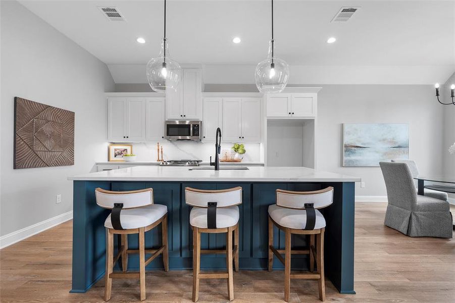 Kitchen featuring white cabinets, light wood finished floors, pendant lighting, a kitchen island with sink, and blue cabinetry Kitchen featuring white cabinets, light wood finished floors, pendant lighting, a kitchen island with sink, and blue cabinetry