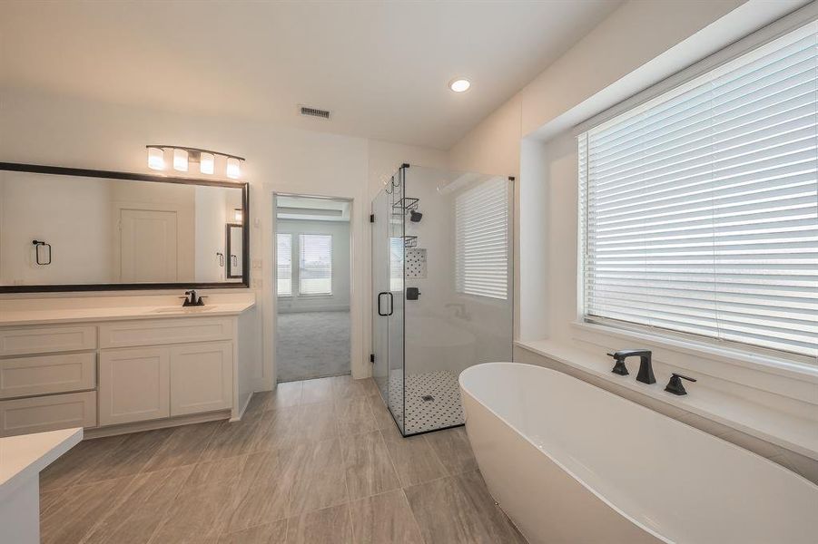 Primary Bathroom featuring a freestanding bathtub, a glass-enclosed shower, a double vanity with a large mirror, and tiled flooring