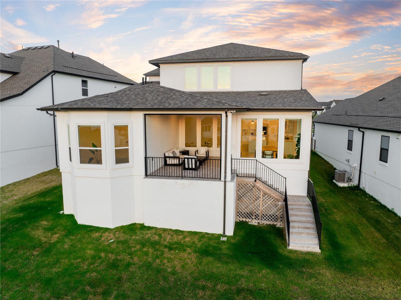 Back of house at dusk with roof with shingles, stairs, and a lawn