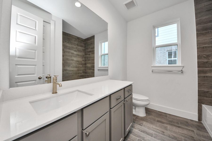 Secondary bath features tile flooring, bath/shower combo with tile surround, light stained wood cabinets, beautiful light countertop.