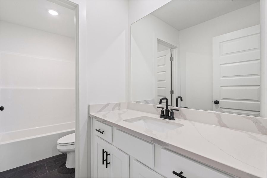 Bathroom featuring a white vanity with black hardware, an integrated sink, and a countertop with subtle veining Bathroom featuring a white vanity with black hardware, an integrated sink, and a countertop with subtle veining