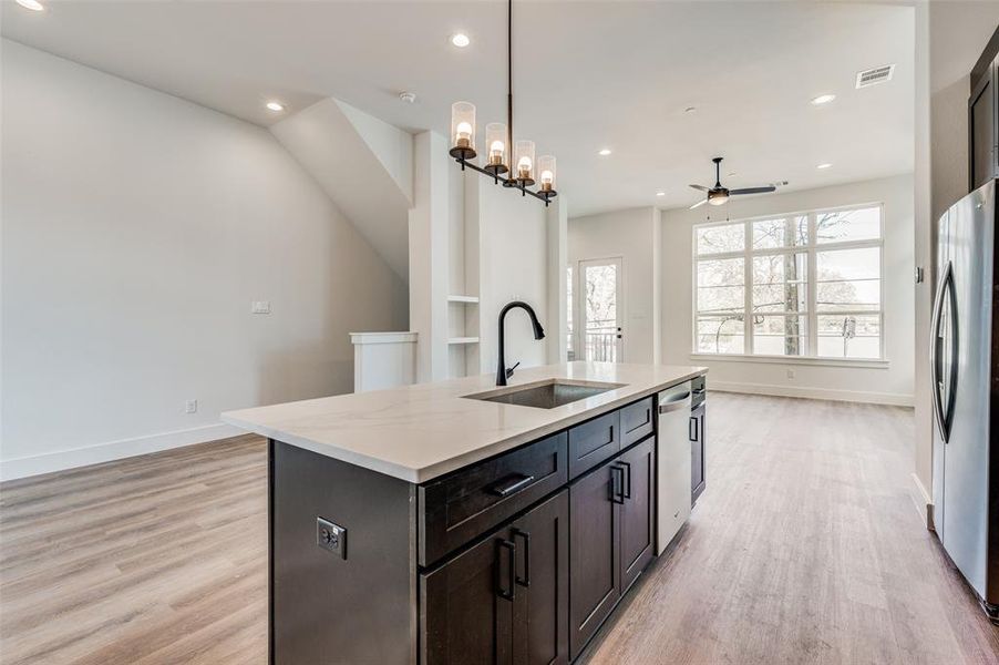 Kitchen with light hardwood / wood-style flooring, a center island with sink, hanging light fixtures, sink, and appliances with stainless steel finishes