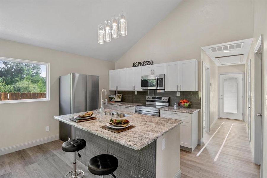 Kitchen featuring lofted ceiling, stainless steel appliances, a breakfast bar, a kitchen island with sink, and light wood-style floors