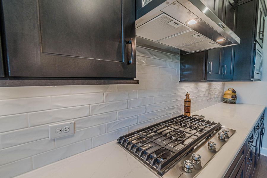 Kitchen featuring stainless steel gas stovetop, ventilation hood, decorative backsplash, and light stone countertops