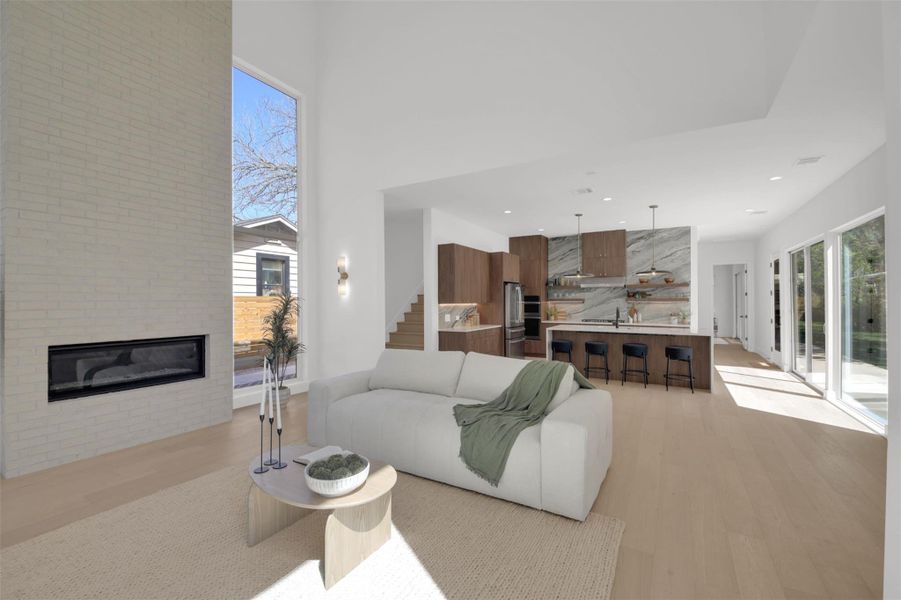 Living area with light wood-style flooring, a glass covered fireplace, healthy amount of natural light, recessed lighting, and a high ceiling