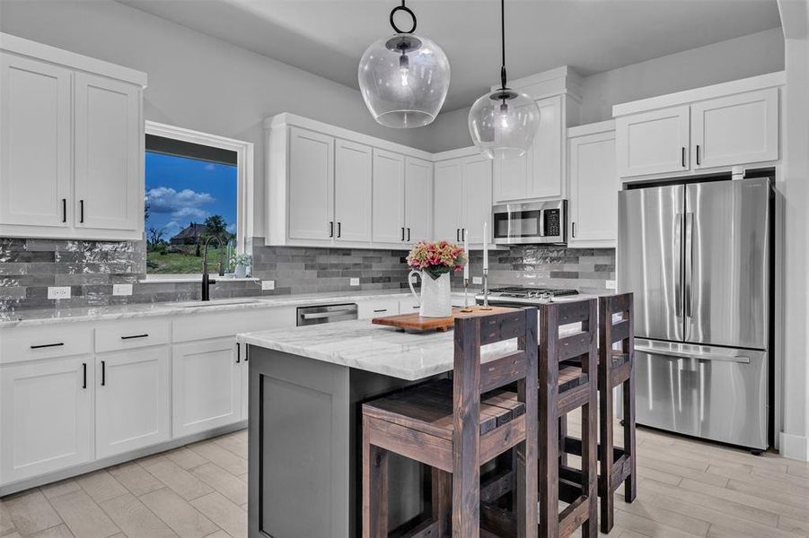 Kitchen featuring an island with seating, pendant lighting, stainless steel appliances, white cabinetry with dark hardware, and light wood-finish flooring