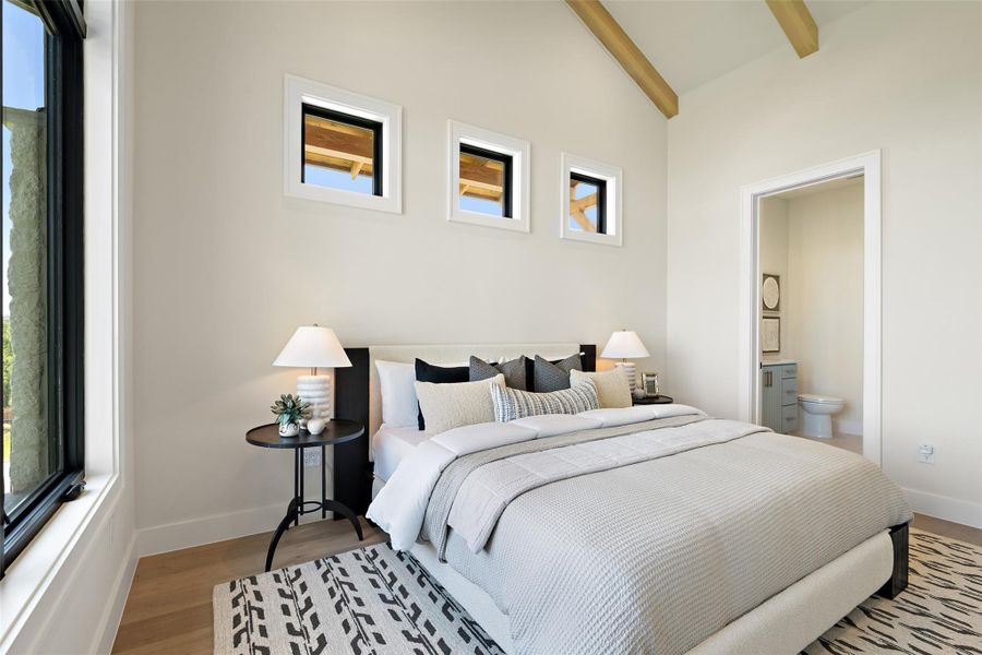Bedroom with beamed ceiling, wood finished floors, connected bathroom, and high vaulted ceiling