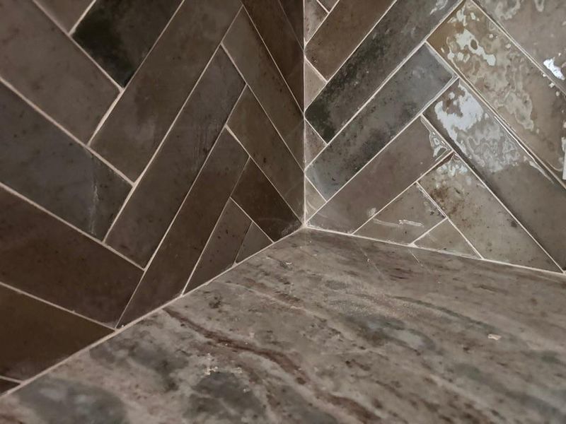 Herringbone pattern wall tile with a variegated glaze, complemented by a stone-finish floor tile