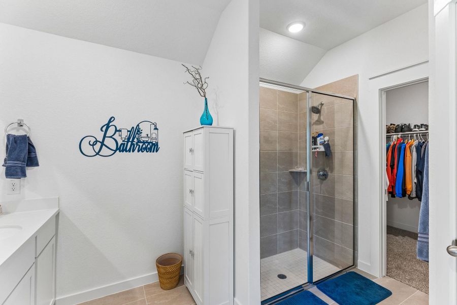 Tiled shower with glass enclosure, white vanity with integrated sink, recessed lighting, and a walk-in closet