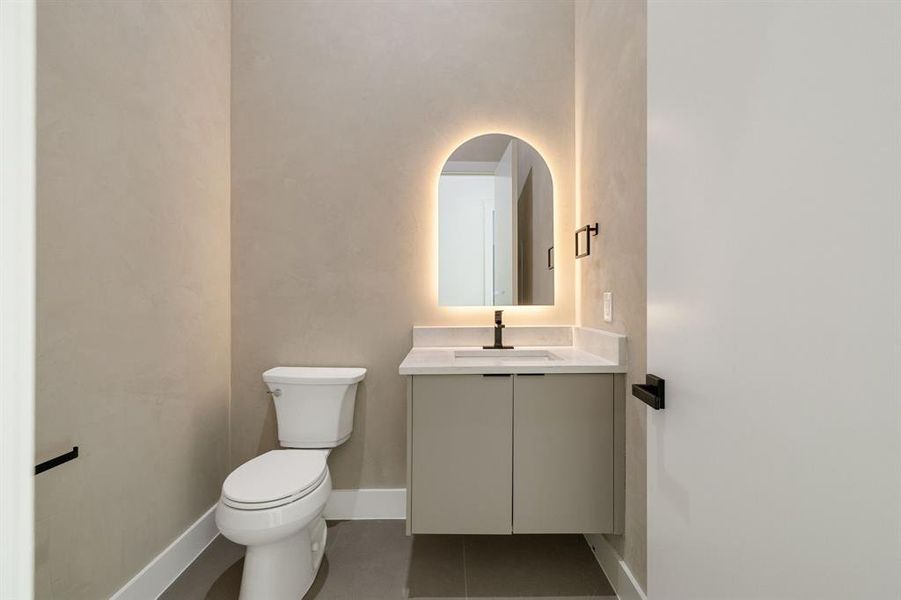 Powder room featuring a sleek vanity with a light countertop, an arched backlit mirror, and a modern wall-mounted faucet
