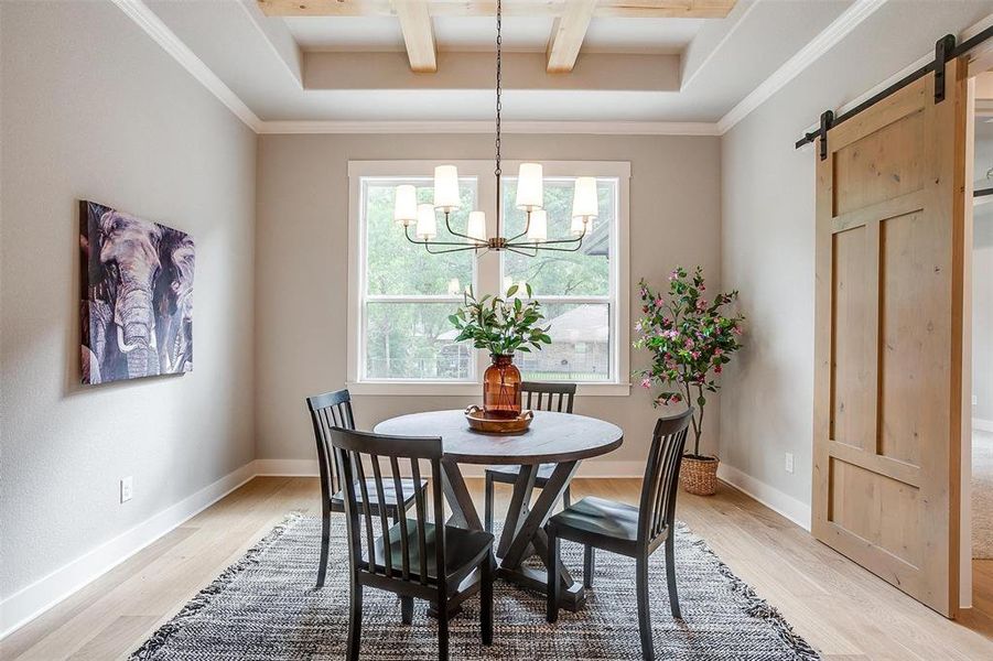 Dining area featuring a barn door, light wood-style flooring, coffered ceiling, a notable chandelier, and beam ceiling Dining area featuring a barn door, light wood-style flooring, coffered ceiling, a notable chandelier, and beam ceiling