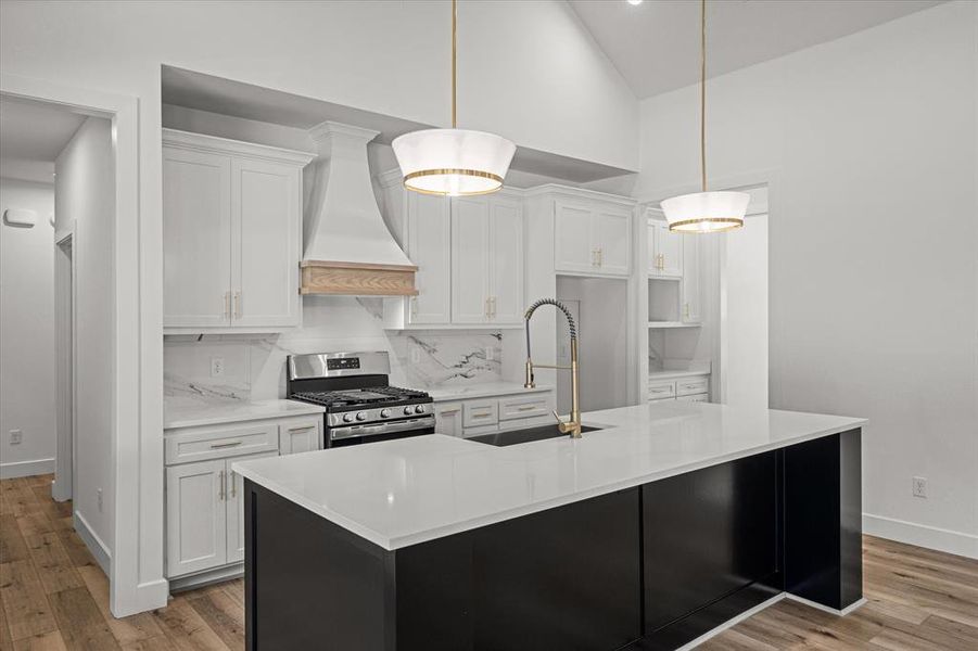 Kitchen featuring dark cabinets, stainless steel range with gas stovetop, white cabinetry, a kitchen island with sink, and premium range hood