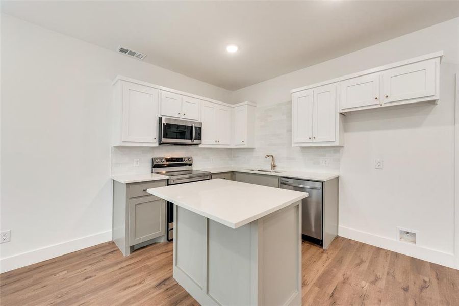 Kitchen featuring decorative backsplash, light wood-type flooring, stainless steel appliances, and a kitchen island