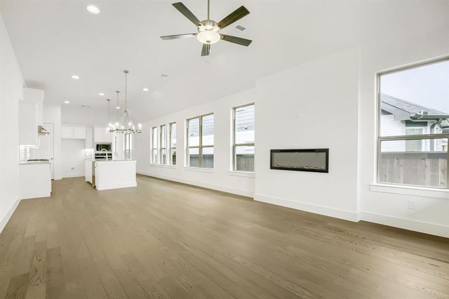 Open-concept living space featuring wood-finish flooring, a linear electric fireplace, multiple windows, recessed lighting, and a ceiling fan