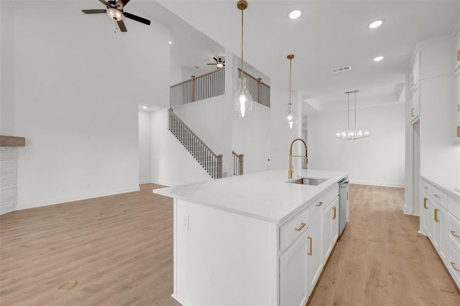 The property features an open-concept layout with light wood flooring and white walls, complemented by a white kitchen island with a gold-toned faucet and pendant lighting