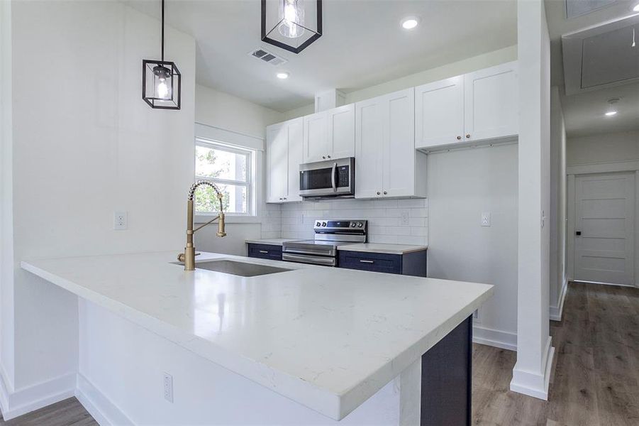 Kitchen featuring a large island with white stone-finish countertop, stainless steel sink, and brass-finish faucet