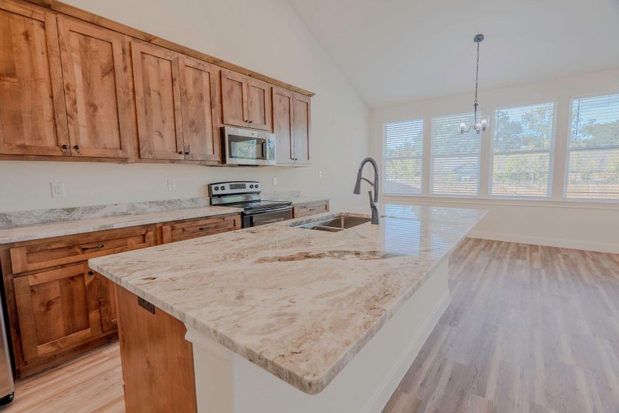 Kitchen with hanging light fixtures, appliances with stainless steel finishes, light wood finished floors, a kitchen island with sink, and light stone counters Kitchen with hanging light fixtures, appliances with stainless steel finishes, light wood finished floors, a kitchen island with sink, and light stone counters