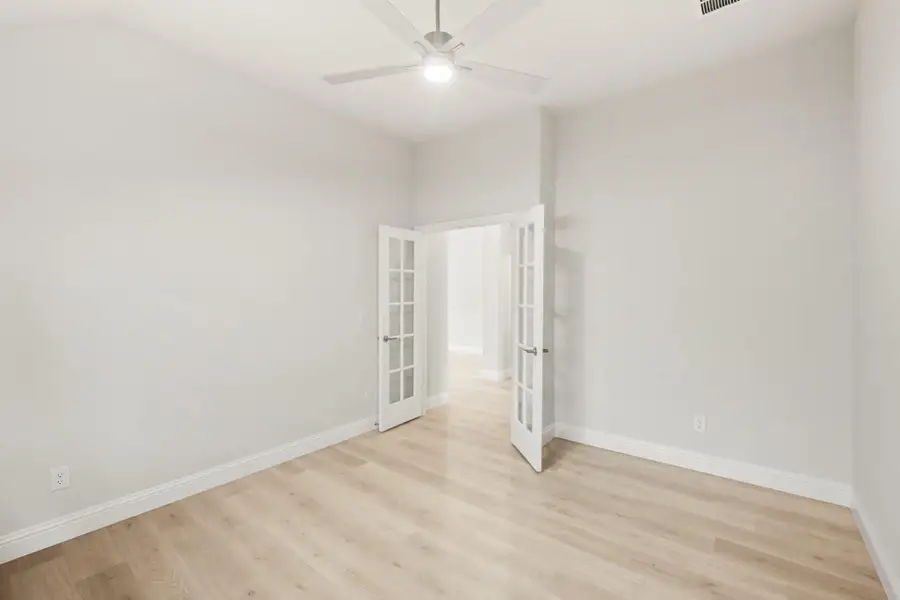 Empty room with light wood floors, ceiling fan, and white French doors Empty room with light wood floors, ceiling fan, and white French doors