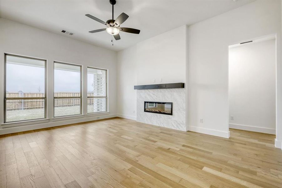 Unfurnished living room with a ceiling fan, light wood-style floors, and a high end fireplace