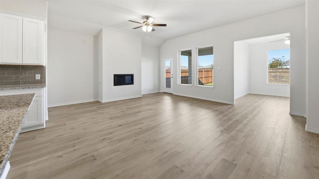 Open-concept living space featuring wood-finish flooring, a built-in electric fireplace, white cabinetry with a tile backsplash, and granite countertops