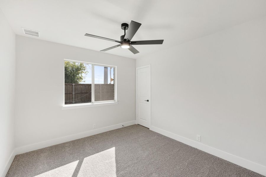 Empty bedroom with gray carpet, white walls, ceiling fan, and single window