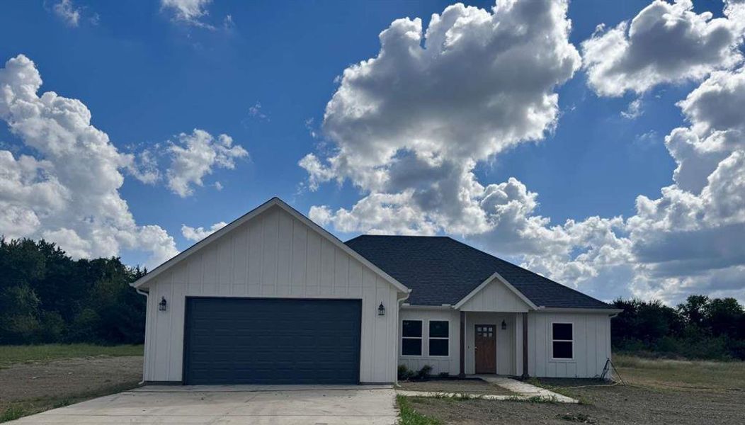 Modern inspired farmhouse with a garage, concrete driveway, roof with shingles, and board and batten siding Modern inspired farmhouse with a garage, concrete driveway, roof with shingles, and board and batten siding
