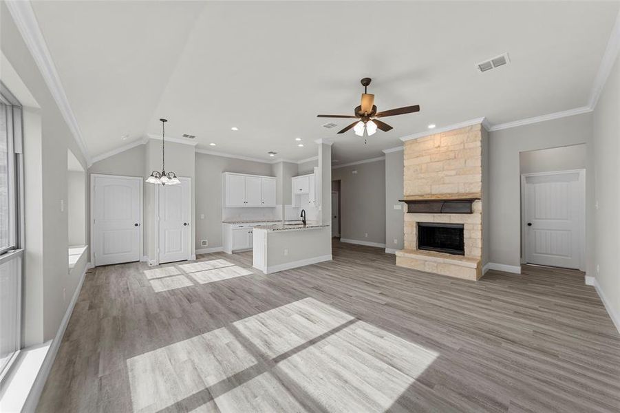 Unfurnished living room featuring lofted ceiling, light hardwood / wood-style flooring, a stone fireplace, and ornamental molding