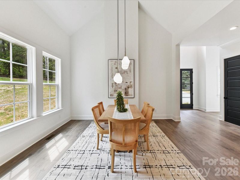 Luminous dining area with vaulted ceilings, large windows overlooking the wooded yard, and modern pendant lighting creating an inviting space for gatherings.