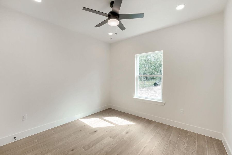 A well-lit bedroom features hardwood flooring and a functional ceiling fan for comfort.
