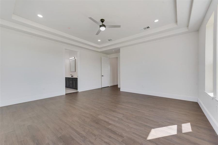 Empty room featuring a raised ceiling, wood-type flooring, and ceiling fan