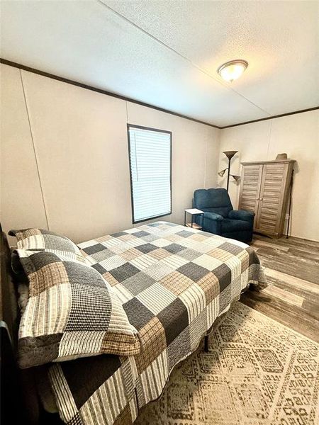 Bedroom with a textured ceiling, wood finished floors, and ornamental molding