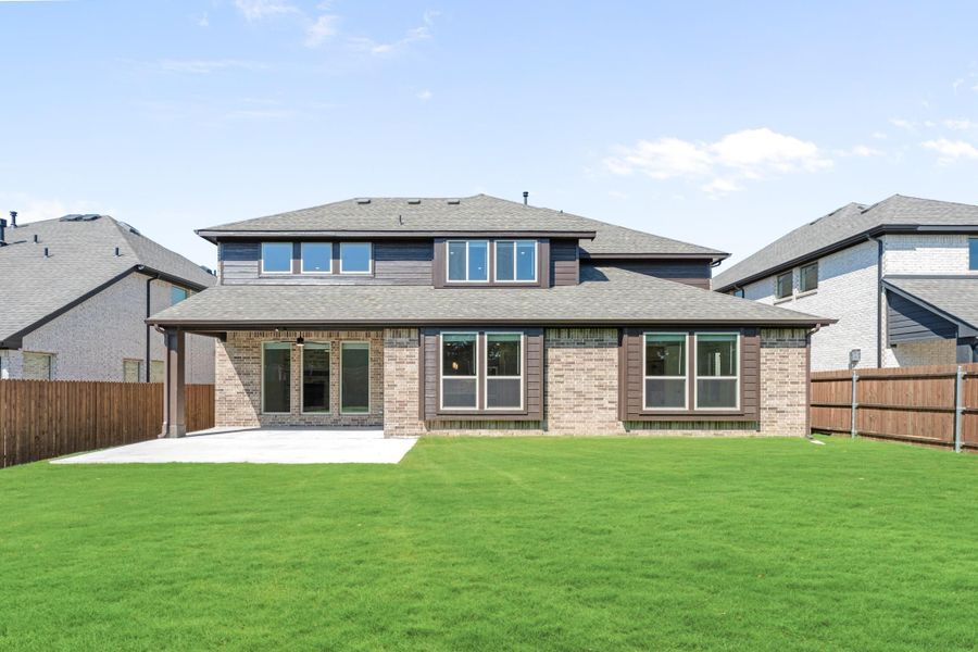 Two-story brick home rear view with covered patio, large windows, and fenced backyard with green lawn