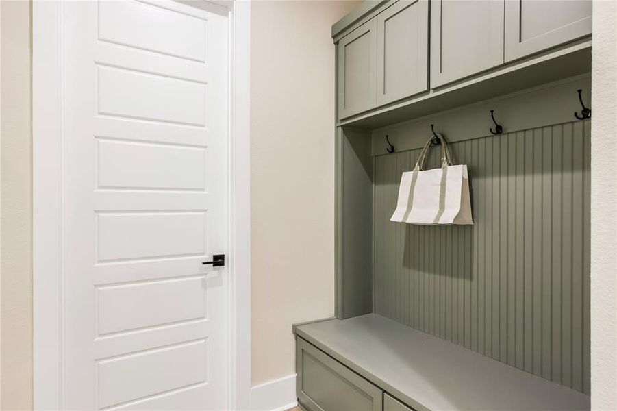 Mudroom with sage green built-in storage and seating, featuring hooks for hanging items. Mudroom with sage green built-in storage and seating, featuring hooks for hanging items.