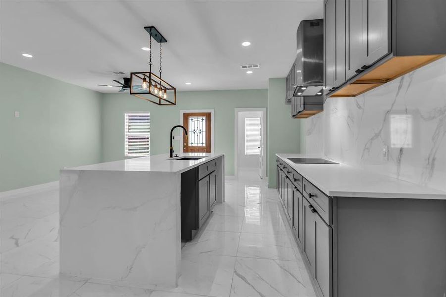 Kitchen with light marble finish flooring, light stone countertops, recessed lighting, hanging light fixtures, and a kitchen island with sink Kitchen with light marble finish flooring, light stone countertops, recessed lighting, hanging light fixtures, and a kitchen island with sink